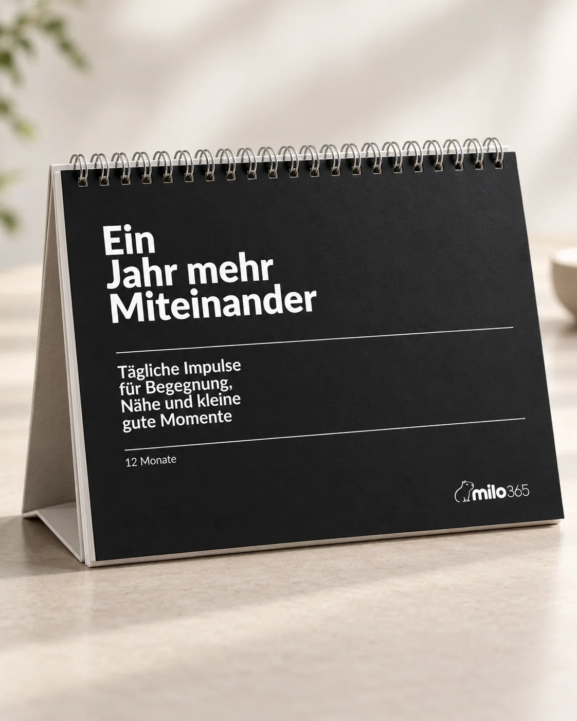 Der Tischkalender „Ein Jahr mehr Miteinander“ mit schwarzem Cover, aufgestellt vor hellem Hintergrund