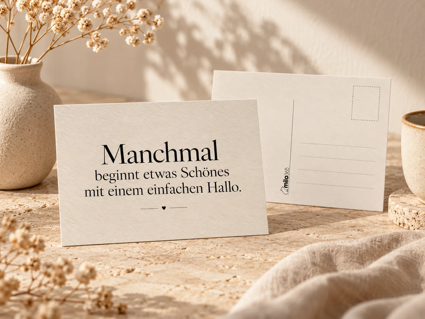 Postkarte „Manchmal beginnt etwas Schönes mit einem einfachen Hallo.“: vorn aufgestellt die Vorderseite, dahinter die Rückseite mit Briefmarkenfeld und Adresslinien